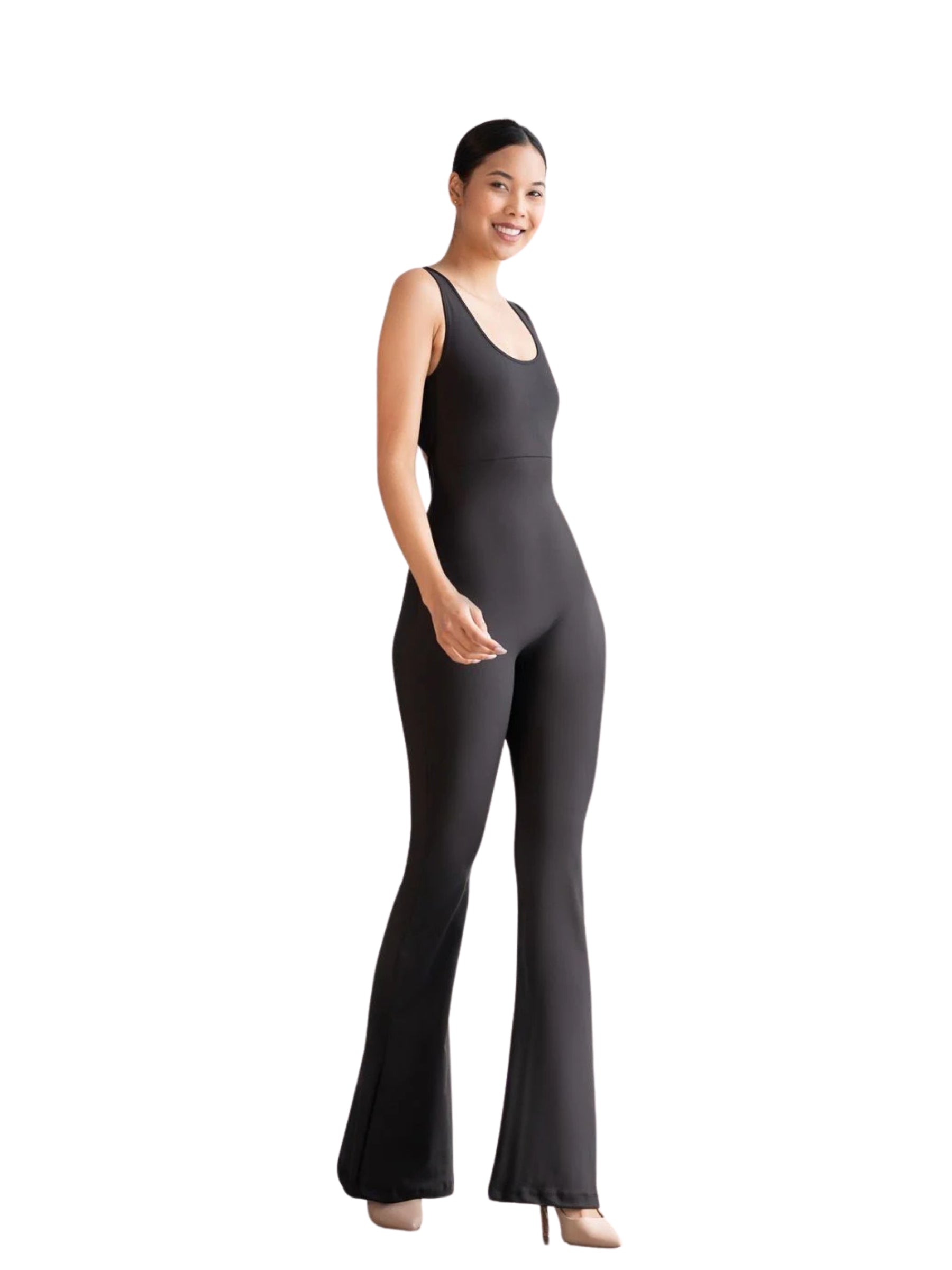 Eine Person trägt einen Lismina 1500 Spanish Scrunch Butt Jumpsuit in Schwarz, mit Absätzen, vor einem weißen Hintergrund und lächelt.